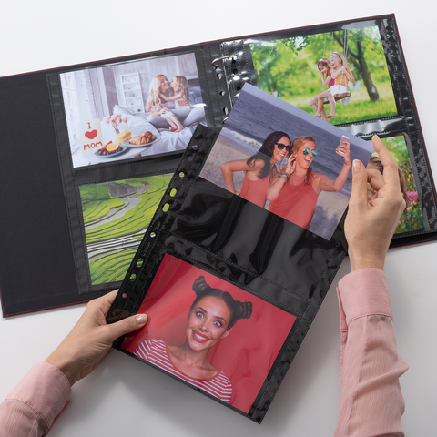 Eine Hand hält ein Fotoalbum mit mehreren Fotos, darunter Porträts von Personen und Landschaften, die in Klarsichthüllen eingelegt sind.