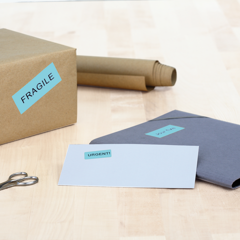 A brown box with a label that says 'FRAGILE,' a gray envelope marked 'URGENT!' and a pair of scissors are lying on a table.