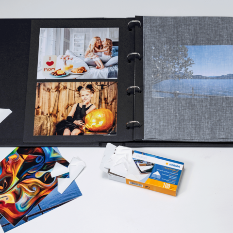 A photo album with several pictures, including portraits and landscapes, as well as some loose postcards and a film packaging.