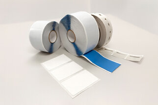 Two rolls of label material, one with a blue surface and one with a white surface, as well as several blank labels on a table.
