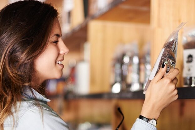 Woman in front of a coffee shelf, image motif for food labeling, landscape format.