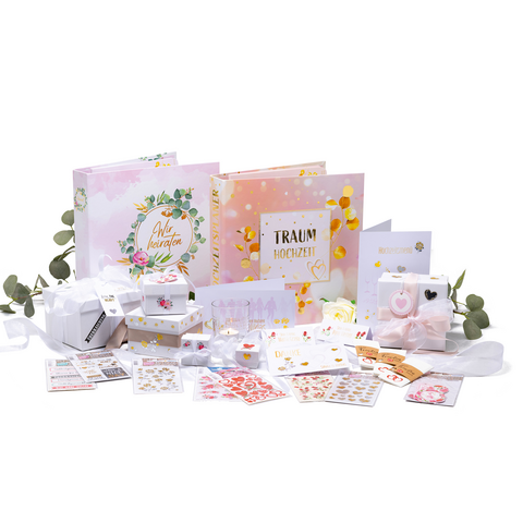 Hochzeitsplanungsset mit zwei Fotoalben, Geschenken, Aufklebern und Dekorationen in Pastellfarben, umgeben von Eukalyptusblättern.