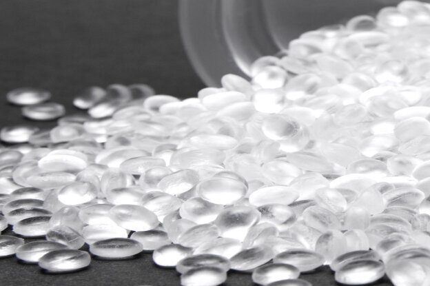 Recycling granulate, also known as recyclate, in front of a container, base material for HERMA film labels, PE and PP, landscape format.