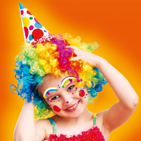 Ein fröhliches Kind mit bunten Locken und Clown-Make-up trägt eine Partyhut und lächelt in die Kamera.