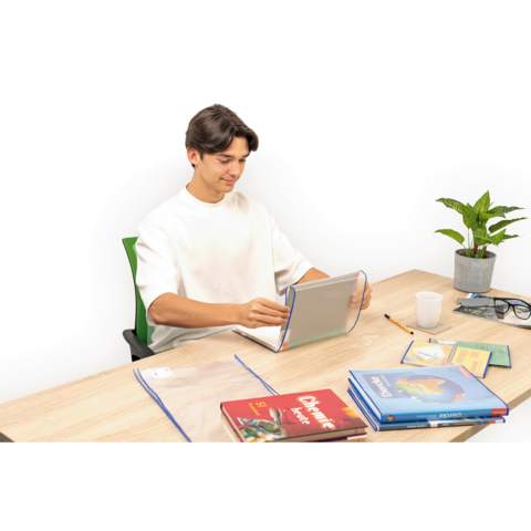 Ein junger Mann sitzt an einem Tisch, nutzt ein Tablet und hat mehrere Bücher sowie Schreibmaterialien vor sich. Eine Pflanze steht daneben.