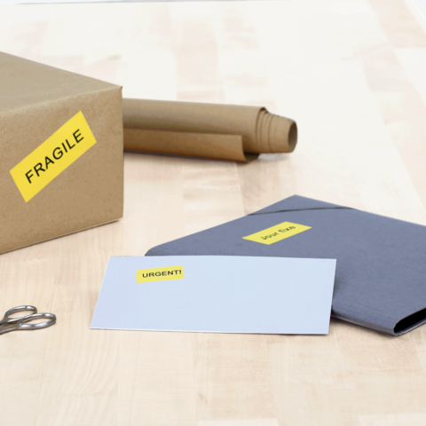 Ein Karton mit dem Aufkleber "FRAGILE", daneben ein graues Kuvert mit der Aufschrift "URGEN!T" und eine Schere.